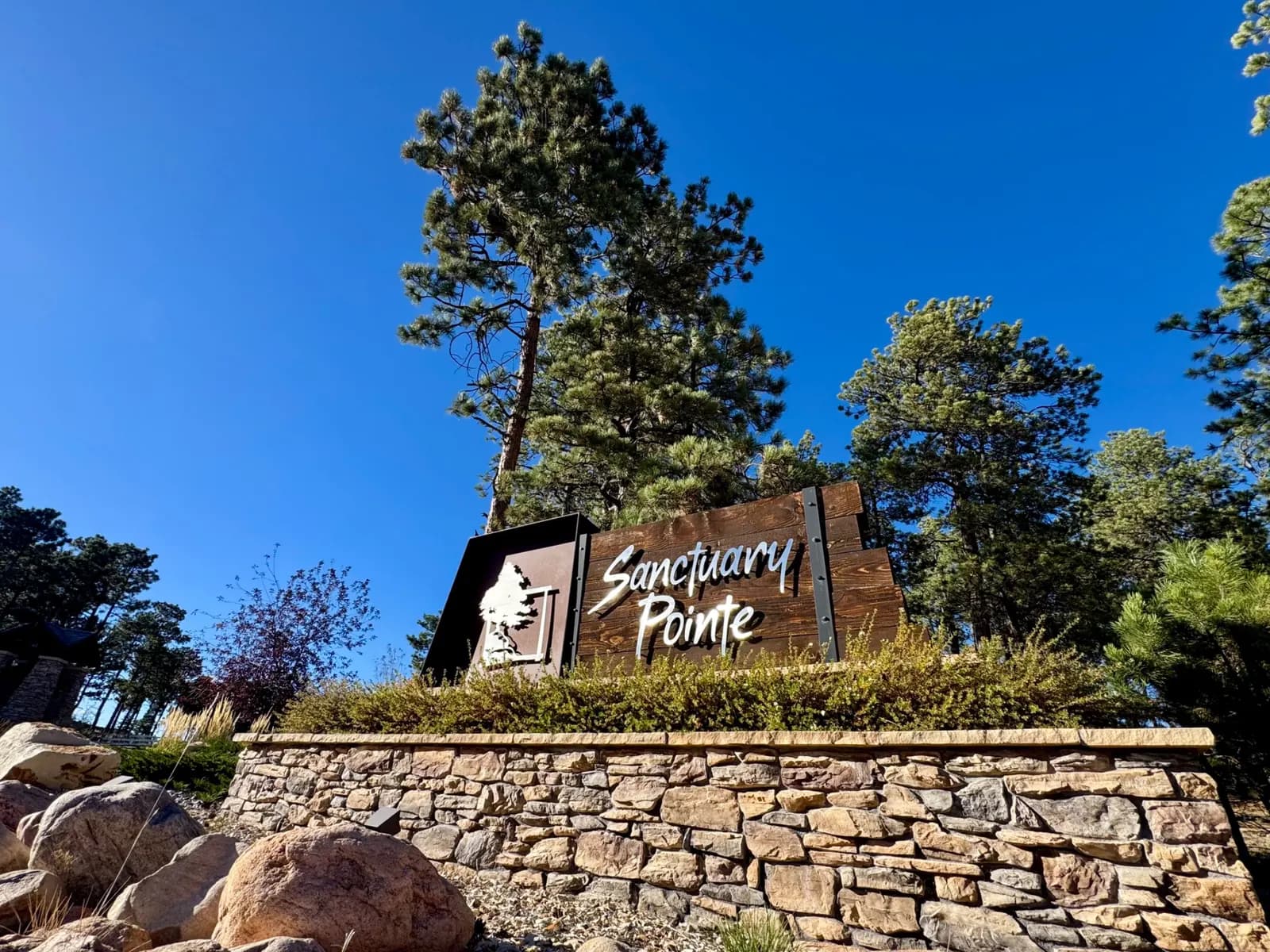 Heather Collection photograph of the Sanctuary Pointe entrance sign on a stone wall among pines.