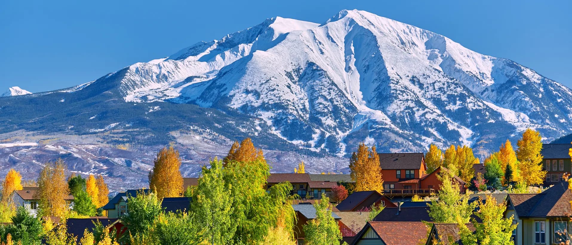 Colorado Springs homes and autumn trees with a snow-covered mountain backdrop